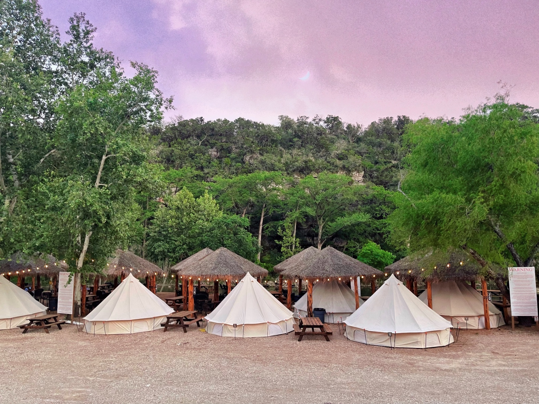 Glamping tents at sunset with tiki huts and string lights